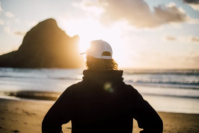 A person facing the sunrise from a quiet shoreline